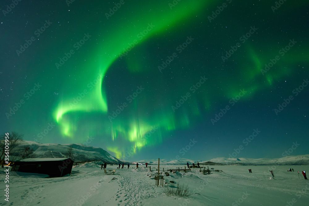 People photographing the northern lights on the frozen lake Torneträsk in Abisko, Sweden