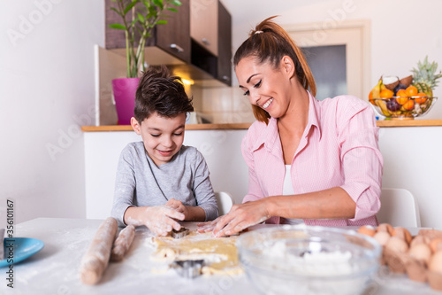 Young mother and cute little son boy preparing the dough, bake cookies and having fun in the kitchen. Happy family are preparing bakery together.