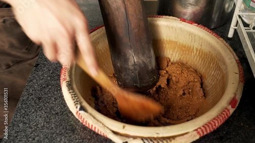 Slow zoom of hand mixing peanut soup ingredients using wooden spoon in pot photo