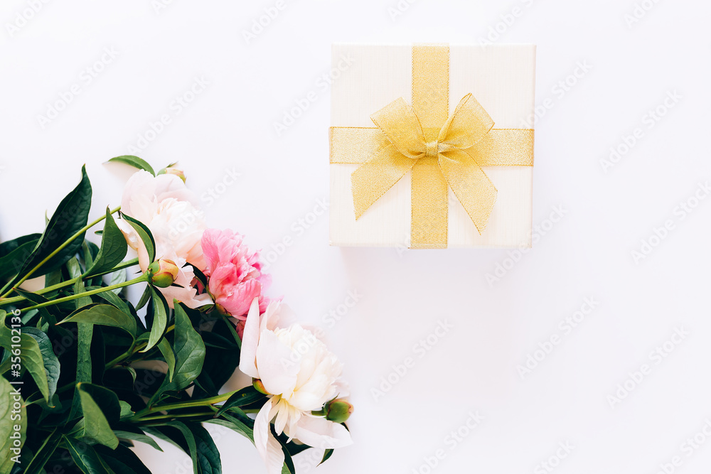 Beautiful bouquet of peonies and a white box with a yellow bow on a white background, flowering peonies