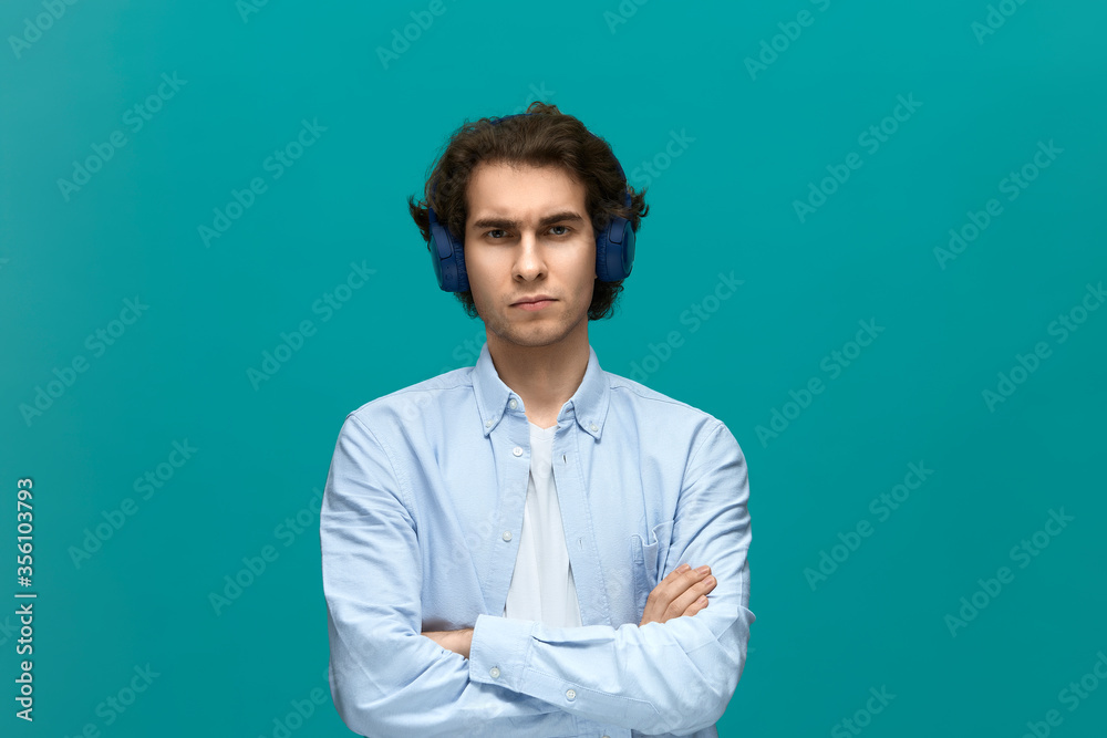 I will not do it. Portrait of a young beautiful man wearing white t-shirt and blue shirt with headphones fold ones arms and looking at camera