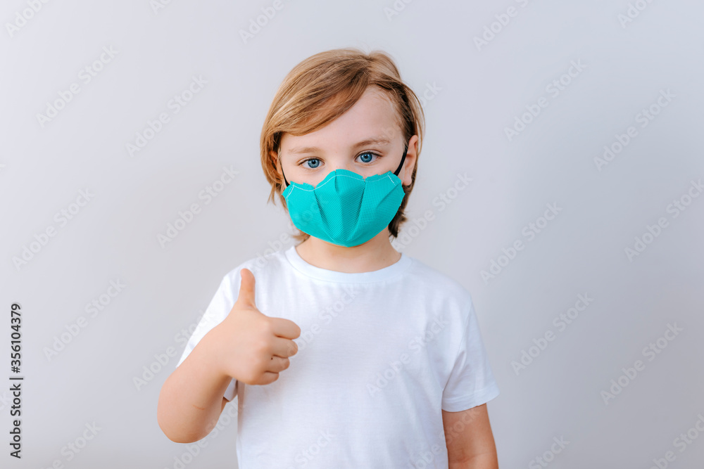 COVID-19 Optimistic kid boy wearing protective mask avoiding Coronavirus disease 2019 showing thumb up in white background. Covid-19 coronavirus COVID-19 Optimistic kid boy wearing protective mask avoiding Coronavirus disease 2019 showing thumb up in white background. Covid-19 coronavirus