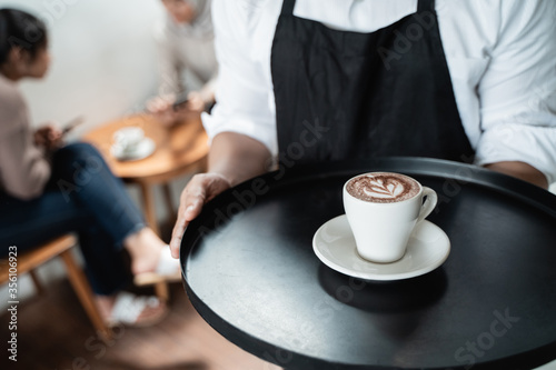 cropped image of waiter serves a cup of coffee on tray to the cafe customer