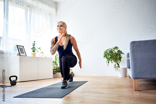Fototapeta Naklejka Na Ścianę i Meble -  Happy athletic woman doing home workout practicing lunges exercise