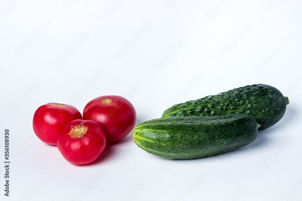 Green cucumbers and tomatoes on a white background. Harvest from the garden. Ingredients for making salad. Green cucumbers and tomatoes on a white background. Harvest from the garden. Ingredients for making salad.