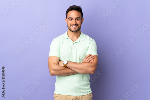 Young handsome man isolated on purple background keeping the arms crossed in frontal position