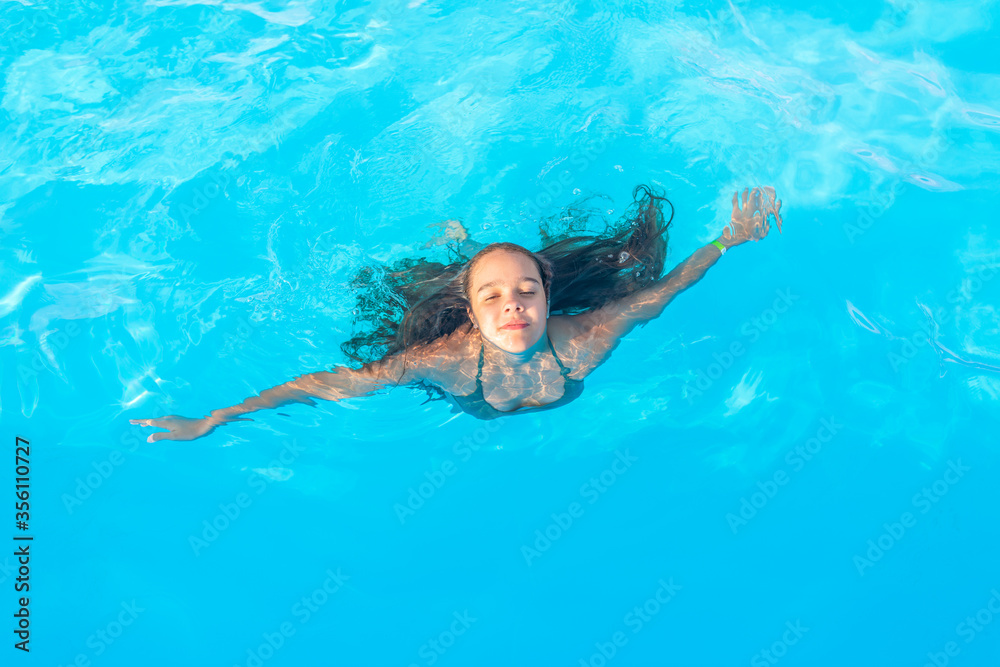 Top view girl teenager swims in the pool in warm clear blue water on sunny summer evening during a vacation in a warm tropical country. Concept recovery and recreation. Advertising space