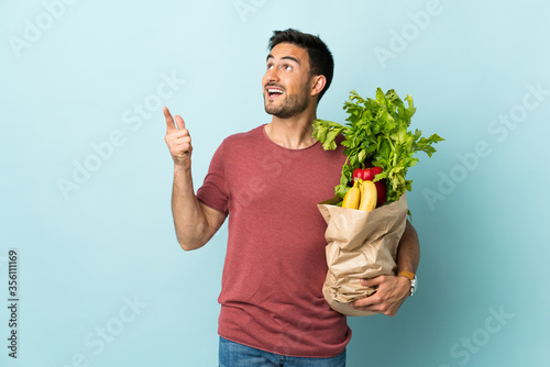 Young caucasian man buying some vegetables isolated on blue background pointing with the index finger a great idea