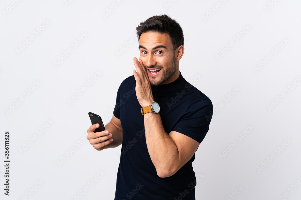 Young caucasian man using mobile phone isolated on white background whispering something Young caucasian man using mobile phone isolated on white background whispering something