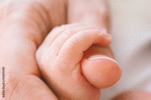 Incredibly cute photo of newborn baby's hand in adult mom's hand. Care, protection and safety of child. Close up. Selective focus.