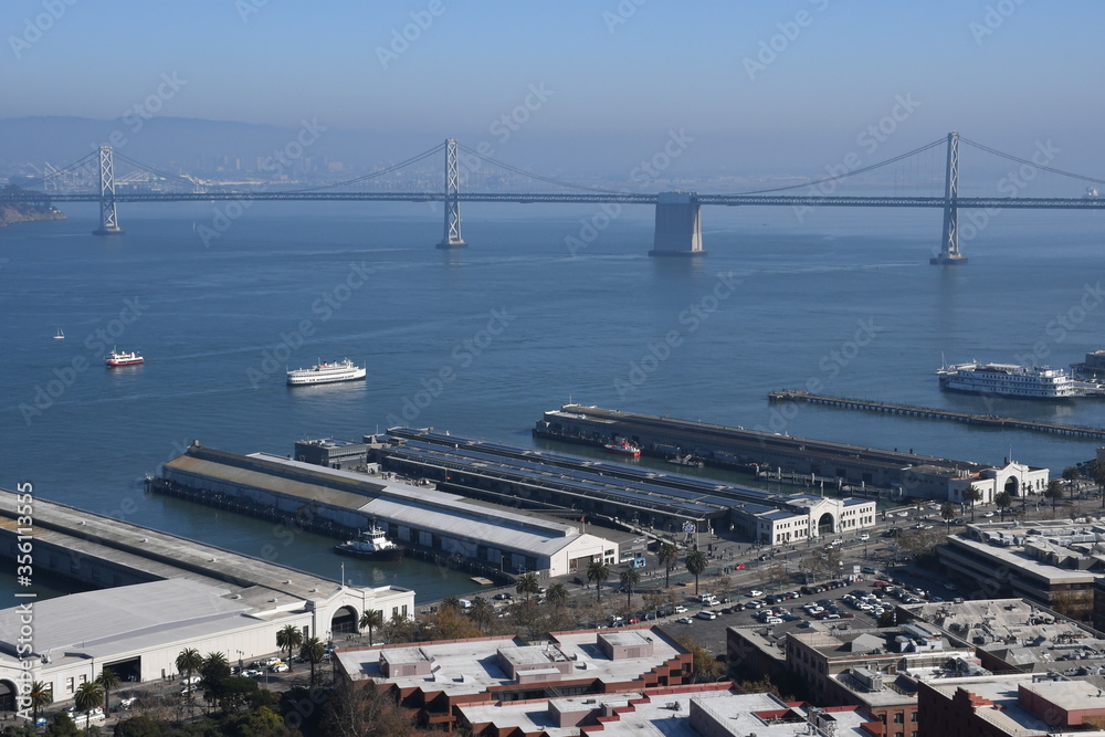 Aerial cityscape of San Francisco Embarcadero and Oakland Bridge from top of Coit Tower on sunny day on Telegraph Hill, California, United States. Aerial cityscape of San Francisco Embarcadero and Oakland Bridge from top of Coit Tower on sunny day on Telegraph Hill, California, United States.