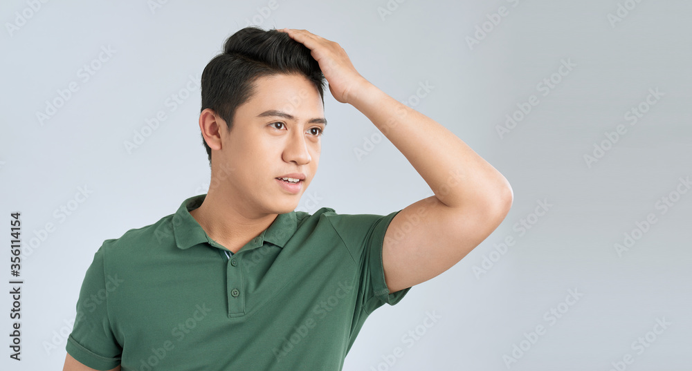 Carefree handsome. Happy young man holding hand in hair and looking away while standing against grey background Carefree handsome. Happy young man holding hand in hair and looking away while standing against grey background