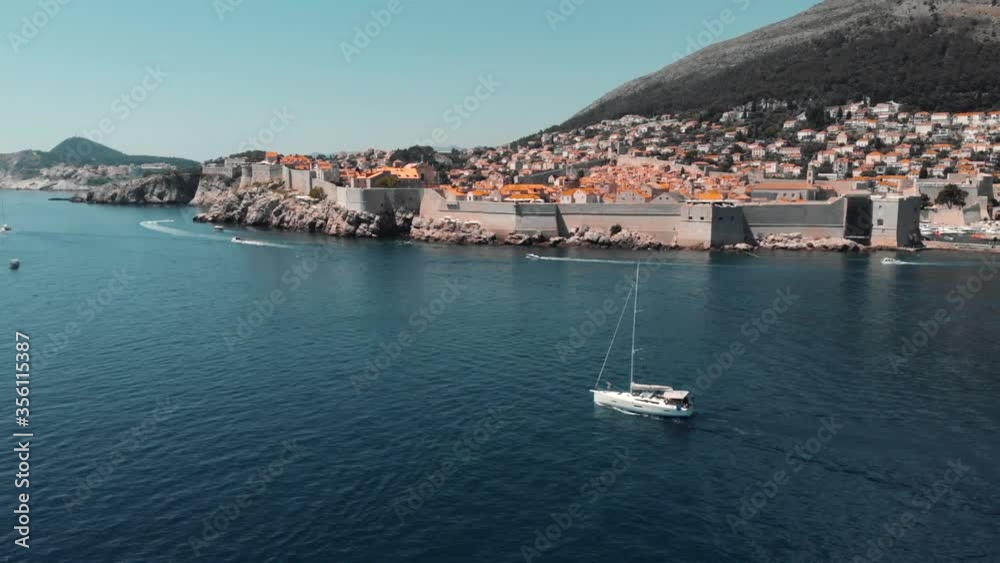 Sailboat floating on sea along coastal town on sunny day Sailboat floating on sea along coastal town on sunny day