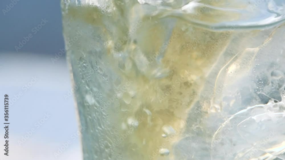Close-up of Air bubble while pouring mineral carbonated water with ice into glass on green nature bokeh background. Close-up of Air bubble while pouring mineral carbonated water with ice into glass on green nature bokeh background.