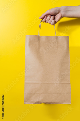 female hand holds a paper bag with goods on a yellow background. buying goods online. goods delivery. Advertising poster.