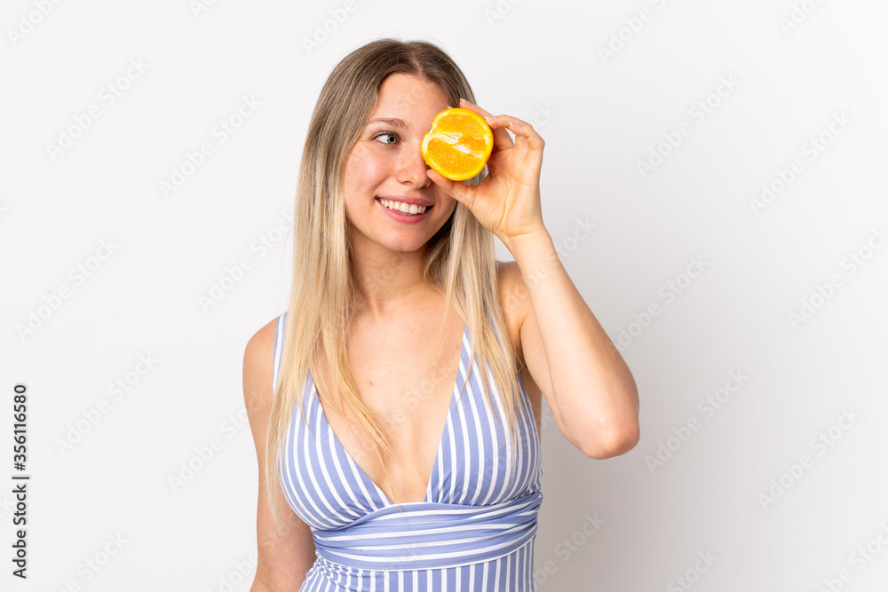 Young blonde woman isolated on white background in swimsuit and holding an orange Young blonde woman isolated on white background in swimsuit and holding an orange