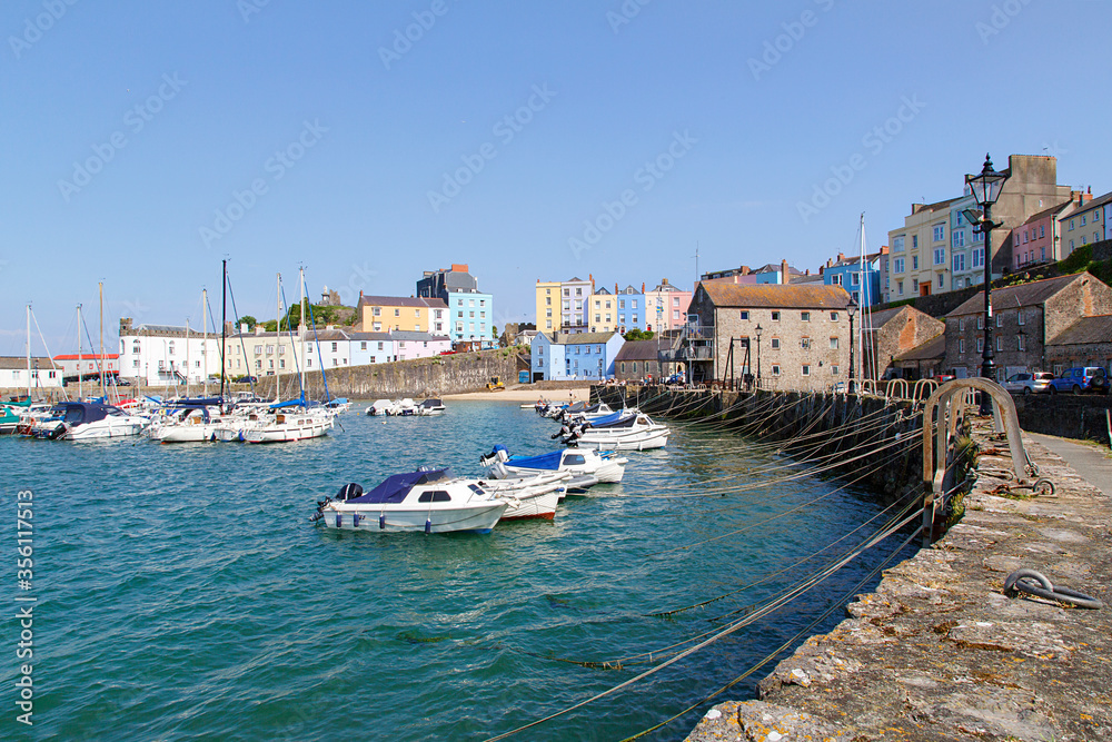 Boats moored in Tenby Harbour at high tide. The harbour is built into a corner of North Beach between the old medieval walled town and castle hill.