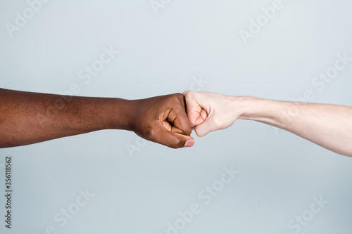 Closeup photo of two arms different race skin colors multinational friends antiracism issue help together buddies world globe integration giving fists bump isolated grey color background
