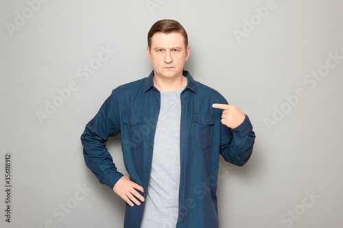 Portrait of serious mature man pointing with index finger at himself