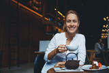 Cheerful female posing with cup of coffee in hand while relax in comfortable restaurant