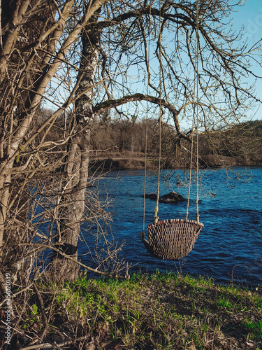Lonely chair swing overlooking a flowing blue river among trees on a cold december morning © Albert