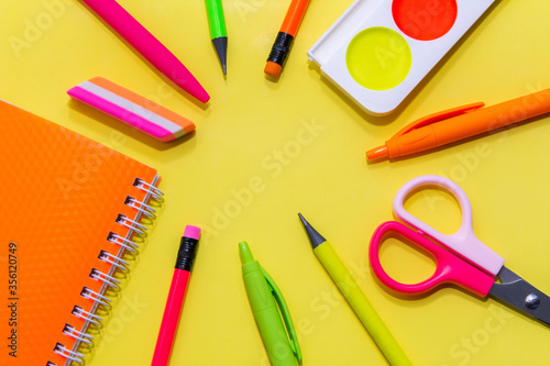 bright color stationery. notebook, pens, scissors, simple pencils, eraser, watercolor paint on an yellow background