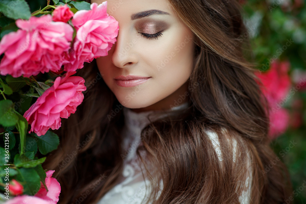 Beautiful portrait of a woman in poses. A brunette woman is standing next to roses in nature.