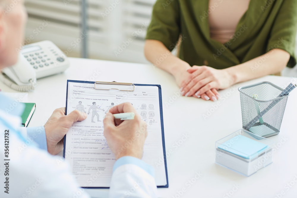 Close up of unrecognizable doctor writing on clipboard and filling patients report while consulting young woman in modern clinic, copy space Close up of unrecognizable doctor writing on clipboard and filling patients report while consulting young woman in modern clinic, copy space