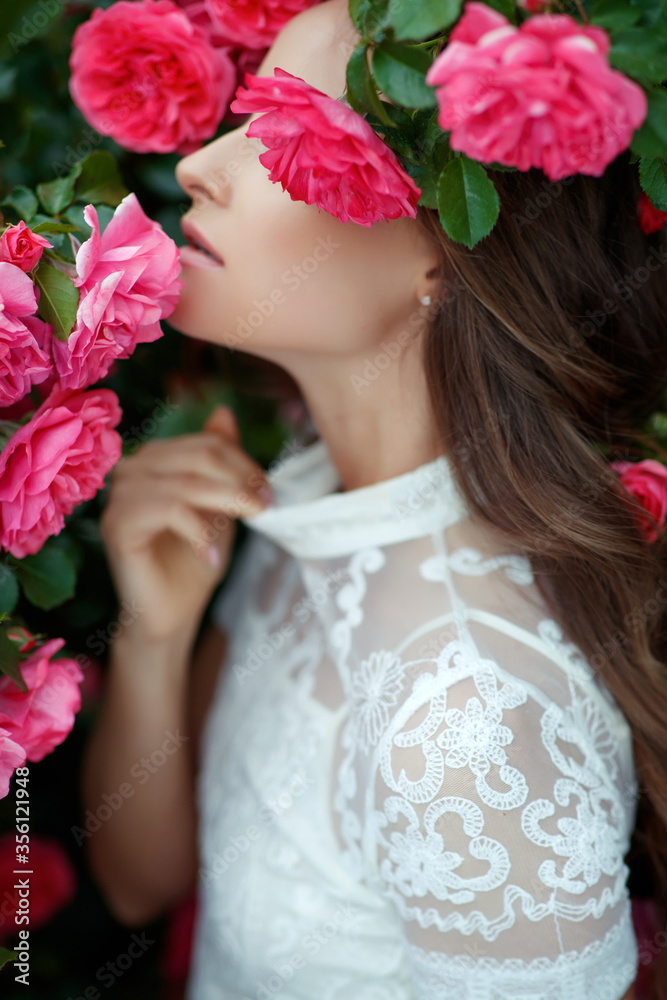Beautiful portrait of a woman in poses. A brunette woman is standing next to roses in nature. Beautiful portrait of a woman in poses. A brunette woman is standing next to roses in nature.