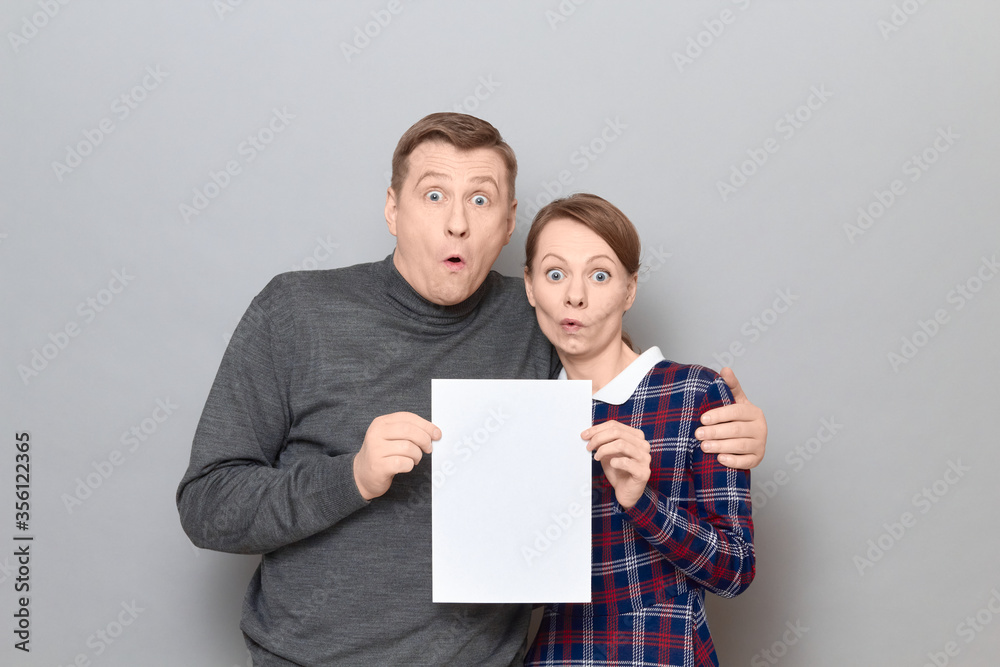 Portrait of adult couple holding together white blank paper sheet Portrait of adult couple holding together white blank paper sheet