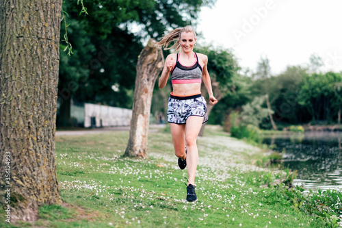 female runner on training outdoor - athlete running on the grass along the river