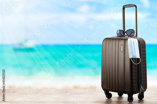 Concept of travel during pandemic . Suitcase with protection mask on the beach