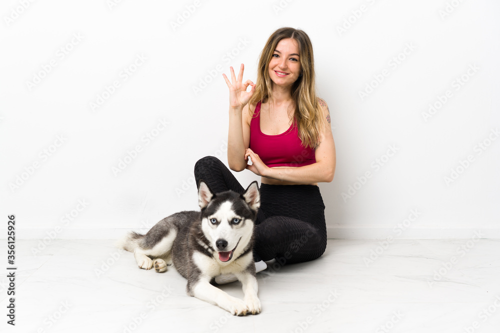 Young sport girl with her dog sitting on the floor showing ok sign with fingers