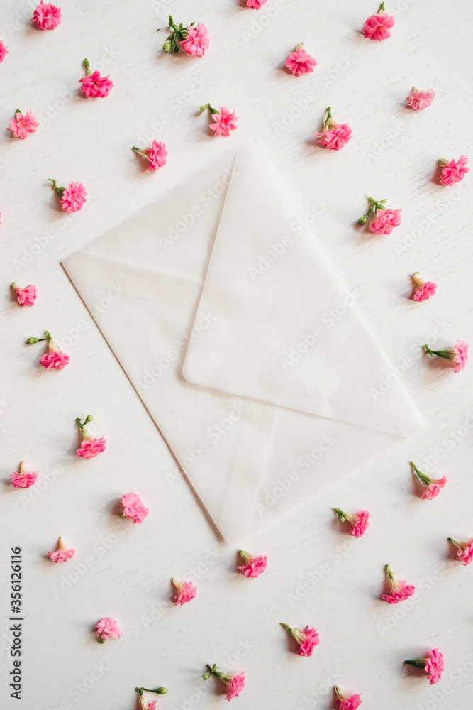 White envelope on a white background with pink little flowers. Greeting card. Creative photo. The flowers are arranged in a row. White envelope on a white background with pink little flowers. Greeting card. Creative photo. The flowers are arranged in a row.