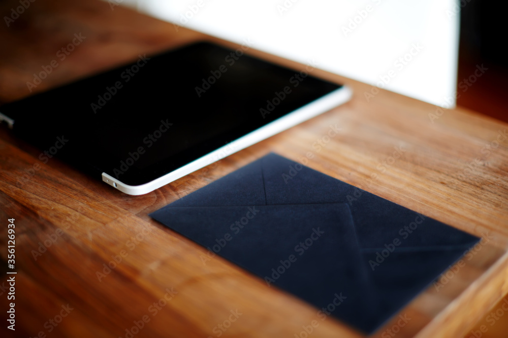 Close up with digital tablet and black envelope on wooden desk in home interior,