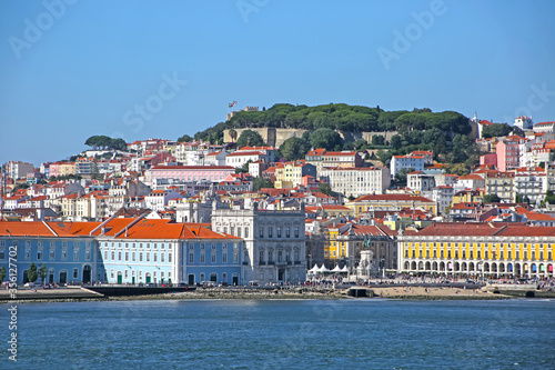 Multi coloured buildings of the old city of Lisbon. São Jorge Castle looking down on the city Praça do Comércio town square in the foreground. View from across the Tagus Estuary, Portugal.