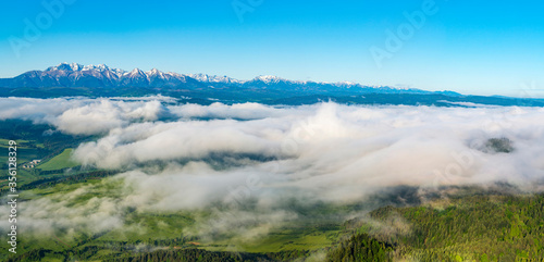 Beautiful wide panorama of the mountain range - Tatra Mountains. Morning fogs and clouds float above the valley. A wonderful spring landscape.
