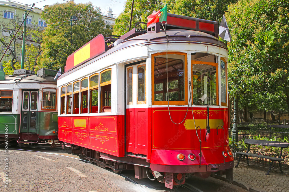 Historic red tram against trees, part of the tramway network since 1873, Lisbon, capital city of Portugal.