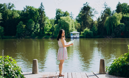 Sofia Park, Uman. Young woman with a tourist map by the lake. A woman in a colored dress walks along the river. Girl on a background of a white gazebo near the lake.