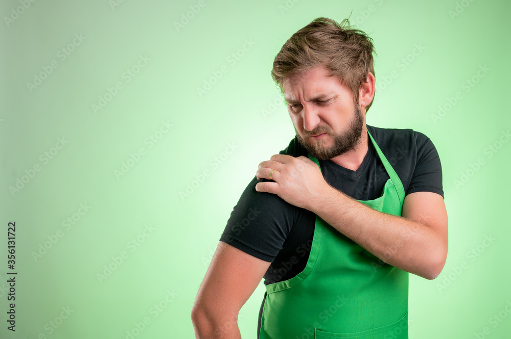Supermarket employee with green apron and black t-shirt has shoulder pain Supermarket employee with green apron and black t-shirt has shoulder pain