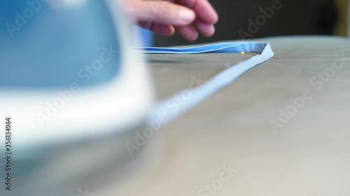 Elderly woman ironing a cotton face mask strap with a yellow pin laying on an ironing board.