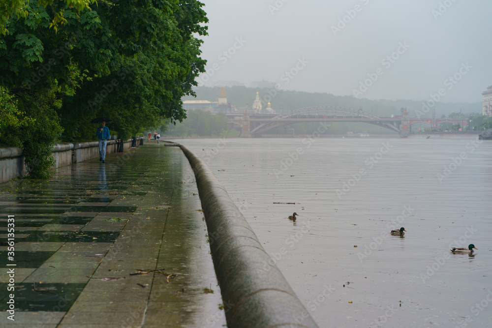 Moskva River embankment, Gorky Park (Neskuchny Garden) - popular place for walking of citizens. Rainy day. Coronavirus pandemic. Andreyevsky railway bridge in distance. Moskva River embankment, Gorky Park (Neskuchny Garden) - popular place for walking of citizens. Rainy day. Coronavirus pandemic. Andreyevsky railway bridge in distance.