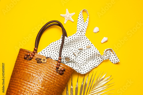 Beach wicker straw or rattan women's eco bag, white dress golden tropical leaf shells starfish on yellow background. Flat lay top view copy space. Concept of travel Summer background Beach accessories