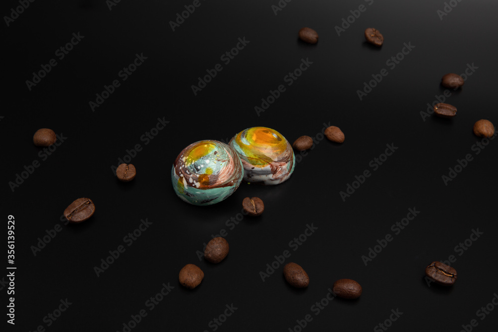 Staked colorful round milk chocolates that looks like planets isolated on black background with copy space, roasted brown coffee beans around them Staked colorful round milk chocolates that looks like planets isolated on black background with copy space, roasted brown coffee beans around them