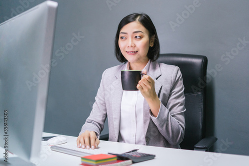 Asian business woman having coffee at her office desk with smiling face.