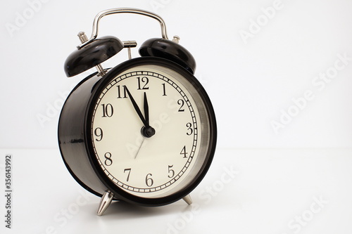 Black vintage alarm clock on table. White background. Wake up concept. An image of a retro clock showing 11:55 pm/am. 