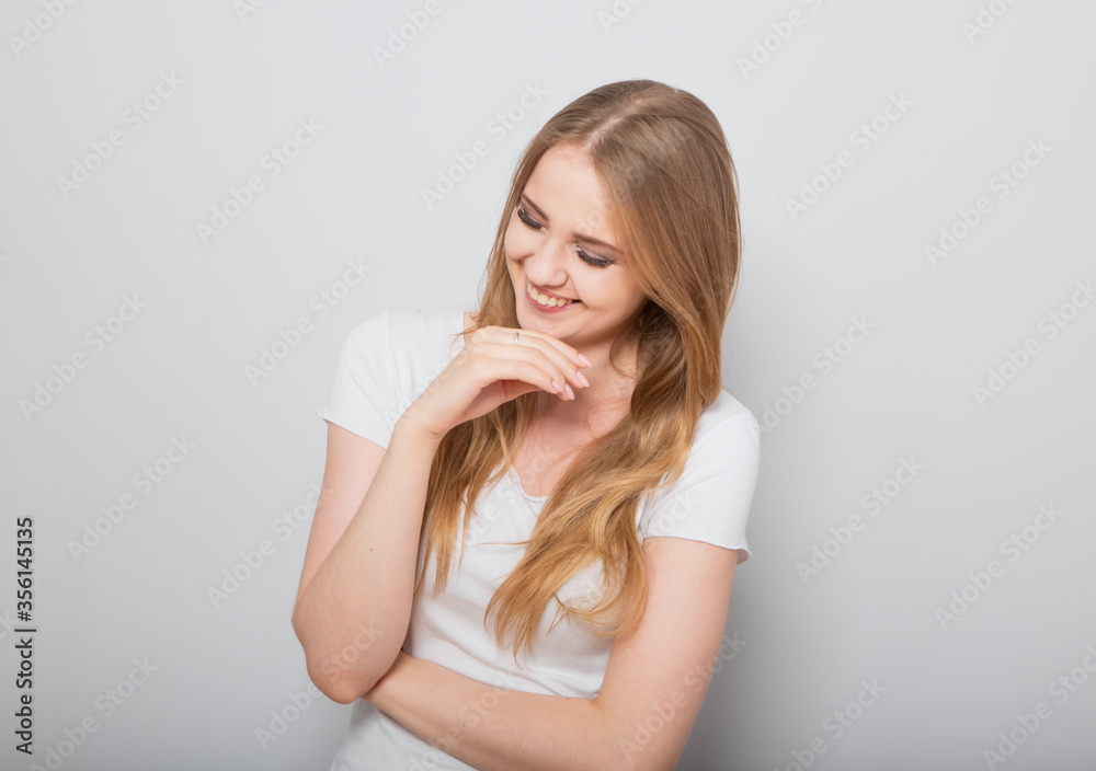 Pretty toothy laughing young woman with fair blond long hair in casual dress holding the head the hands. Studio shot of good looking beautiful woman isolated against grey studio wall Pretty toothy laughing young woman with fair blond long hair in casual dress holding the head the hands. Studio shot of good looking beautiful woman isolated against grey studio wall