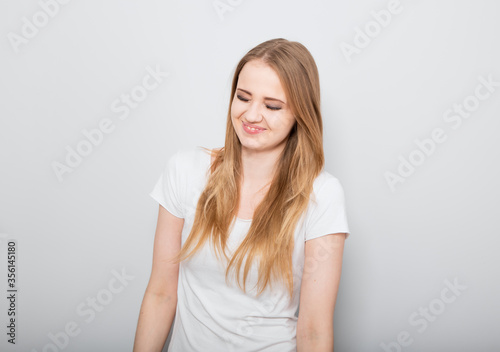 Pretty smiling joyful young woman with fair blond long hair in casual dress looking with happy. Studio shot of good looking beautiful woman isolated against grey studio wall