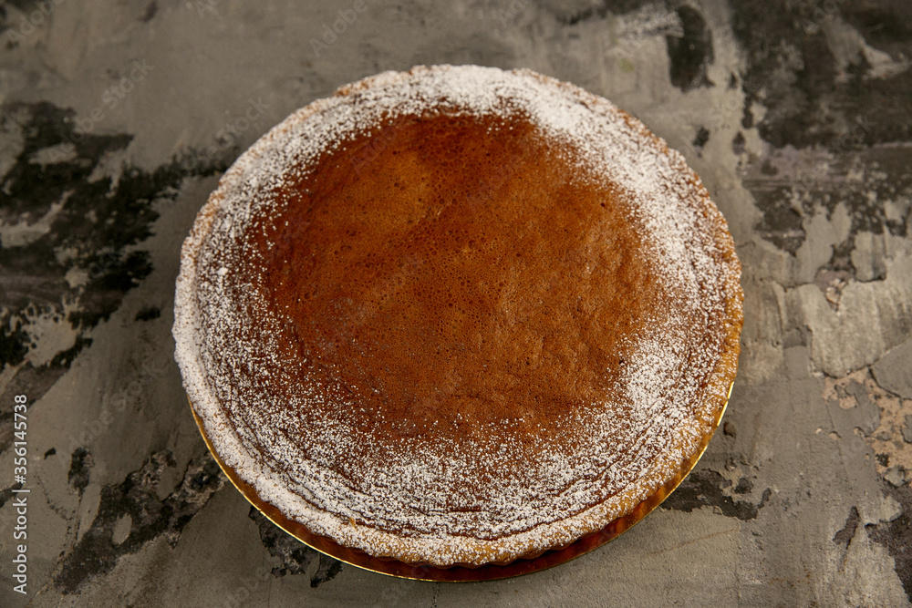 Round chocolate cake with icing sugar on a dark textured concrete background Round chocolate cake with icing sugar on a dark textured concrete background
