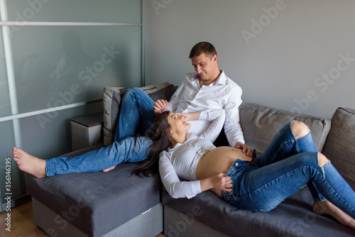 A man and a pregnant woman. Future parents at home. The woman lay on the foot of her husband.